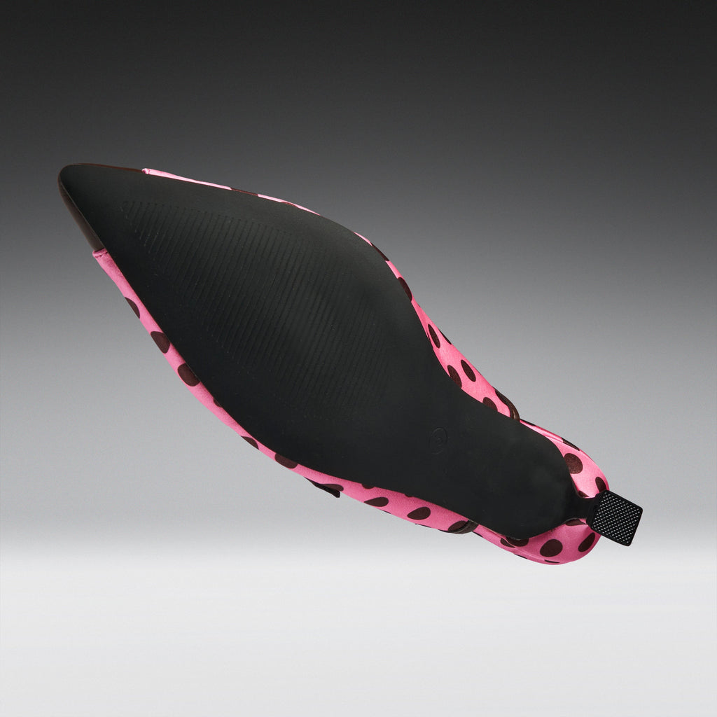 A single pointed-toe shoe shown floating against a dark-to-light gray gradient background. The upper is black with a pink and black spotted pattern around the edges and heel.