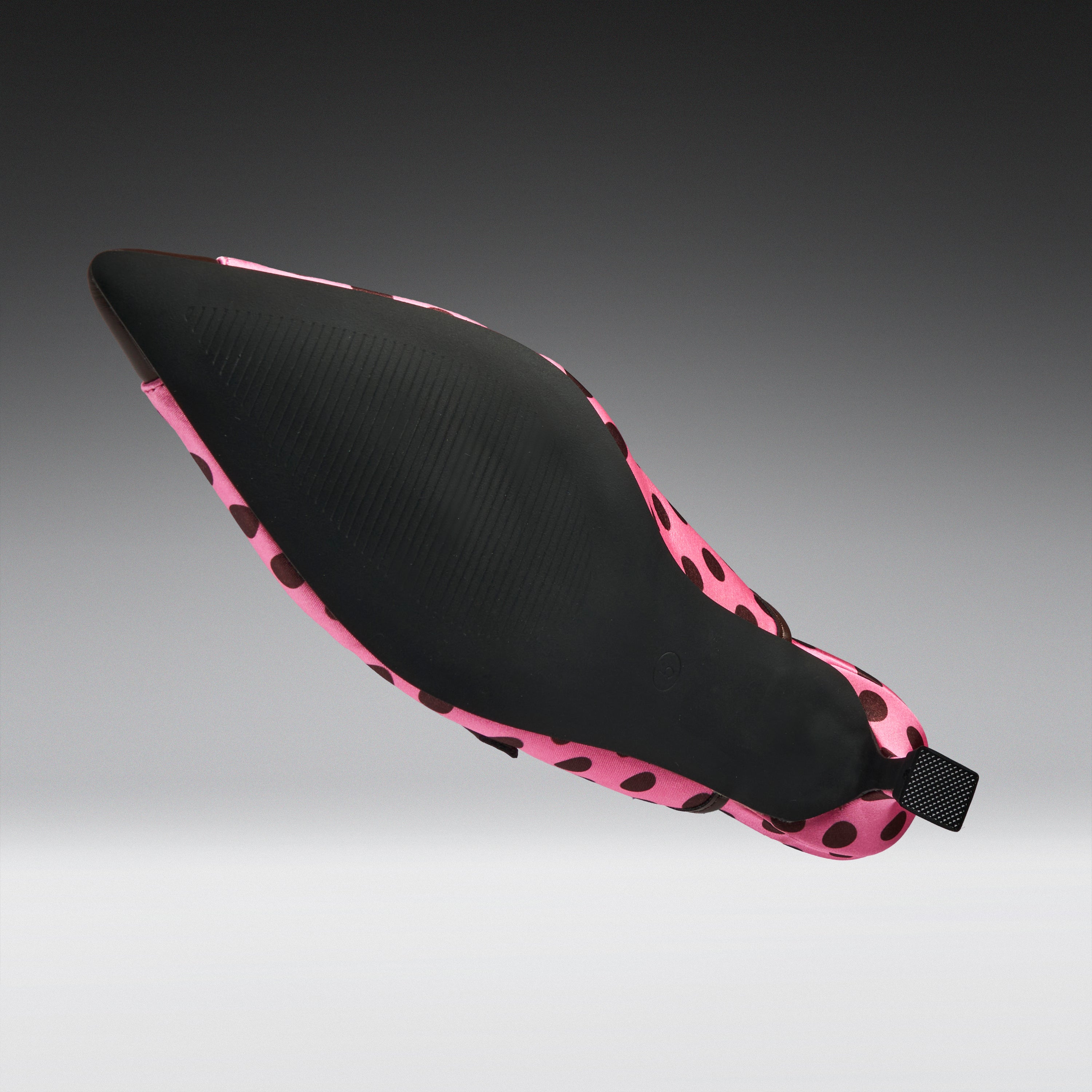 A single pointed-toe shoe shown floating against a dark-to-light gray gradient background. The upper is black with a pink and black spotted pattern around the edges and heel.
