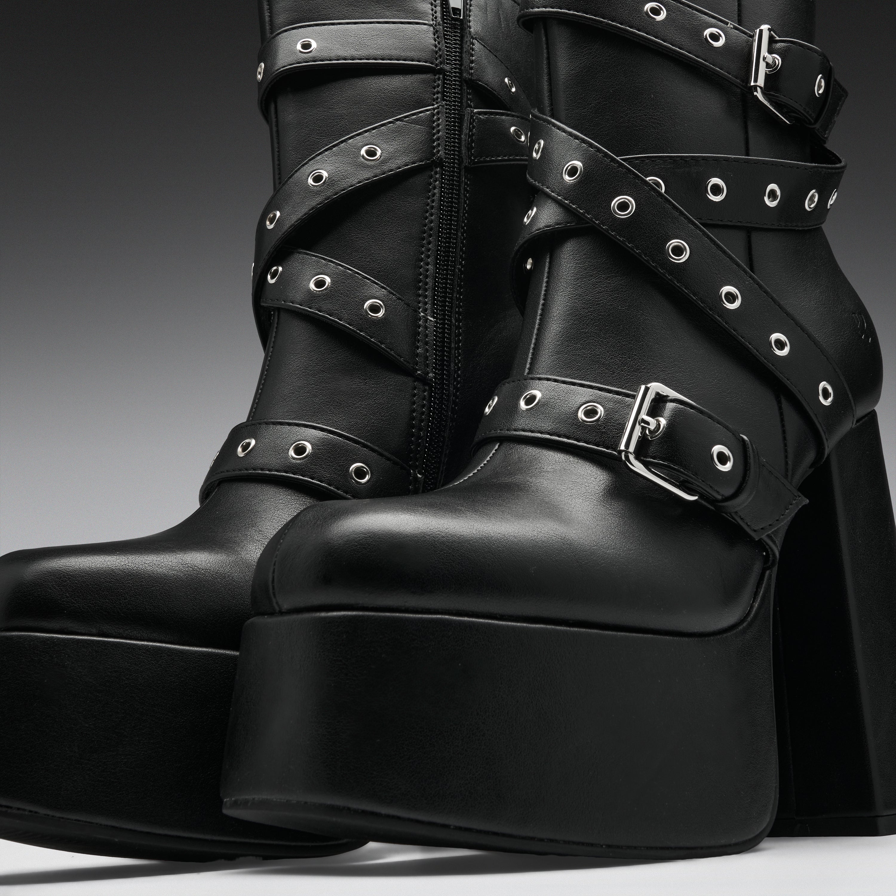Black leather platform ankle boots with multiple wraparound straps, silver-tone eyelets, and chunky block heels, shown in a studio close-up.