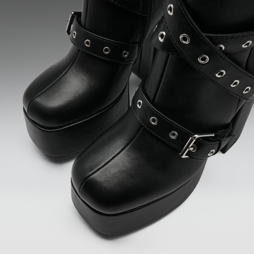 Black platform boots with multiple decorative straps, silver-tone grommets, and buckles, shown in a close-up studio shot.