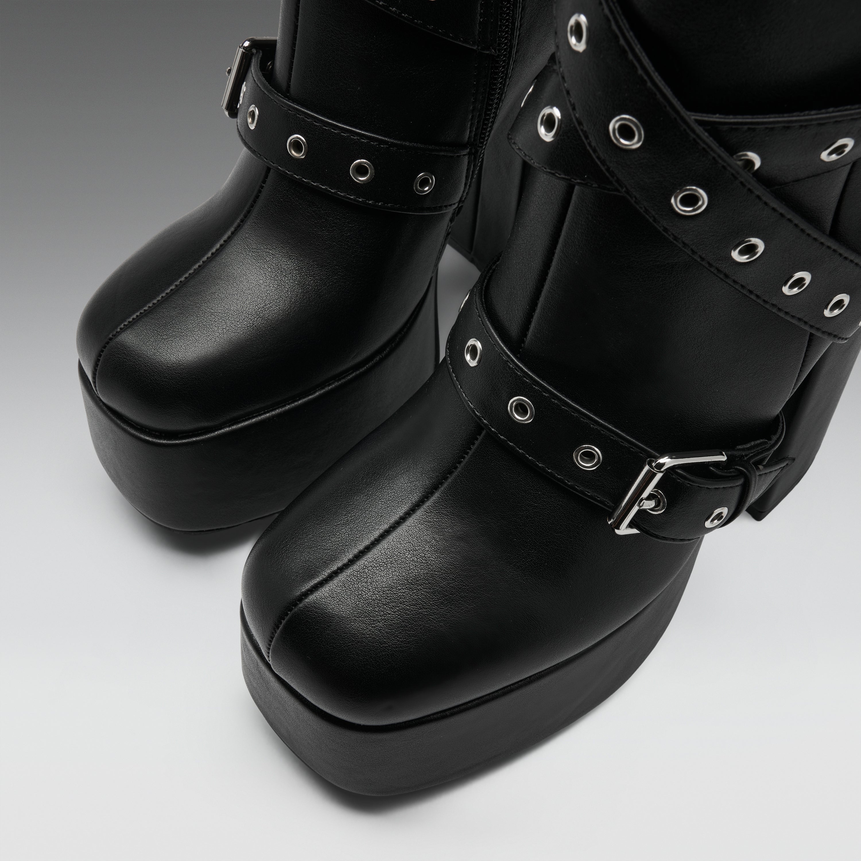 Black platform boots with multiple decorative straps, silver-tone grommets, and buckles, shown in a close-up studio shot.