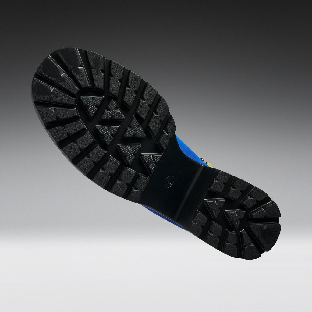 A close-up of a black rubber boot sole with deep tread patterns, shown against a dark gray to light gray gradient background.
