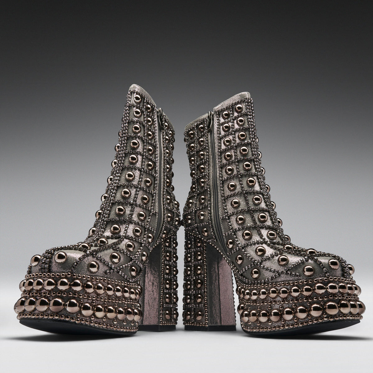A pair of heavily embellished platform ankle boots with metallic rose gold studs and rhinestone detailing, shown from the side against a dark gray gradient background.