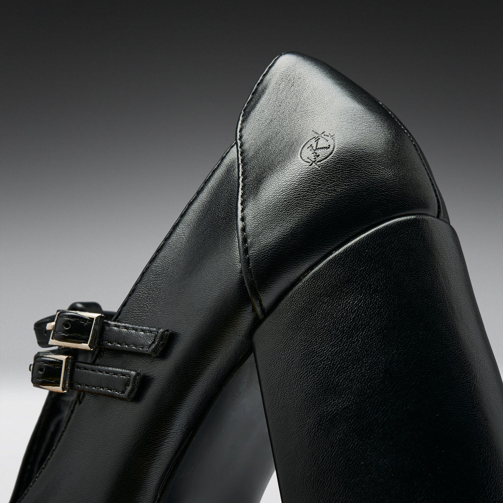 Close-up of a black leather boot with double buckle straps and a small embossed logo on the heel, photographed against a dark gray gradient background.