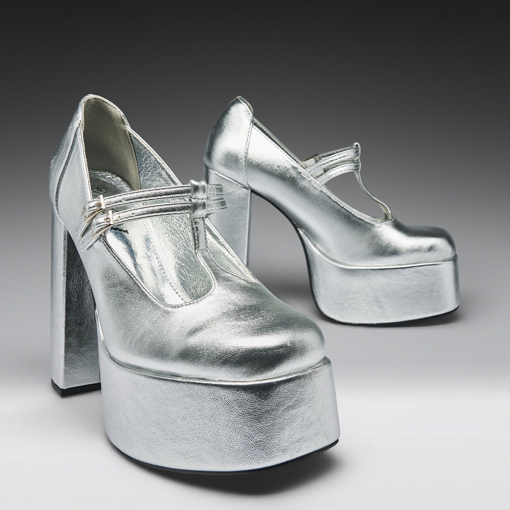 A pair of metallic silver platform Mary Jane high heels with block heels and ankle straps, photographed on a dark-to-light gray gradient studio background.