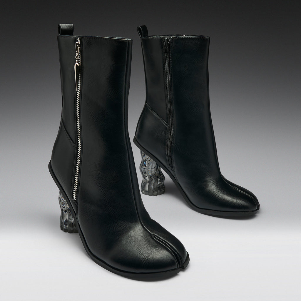A pair of black leather ankle boots with a distinctive split toe and sculptural clear resin animal-head heels, shown against a dark gray studio background.