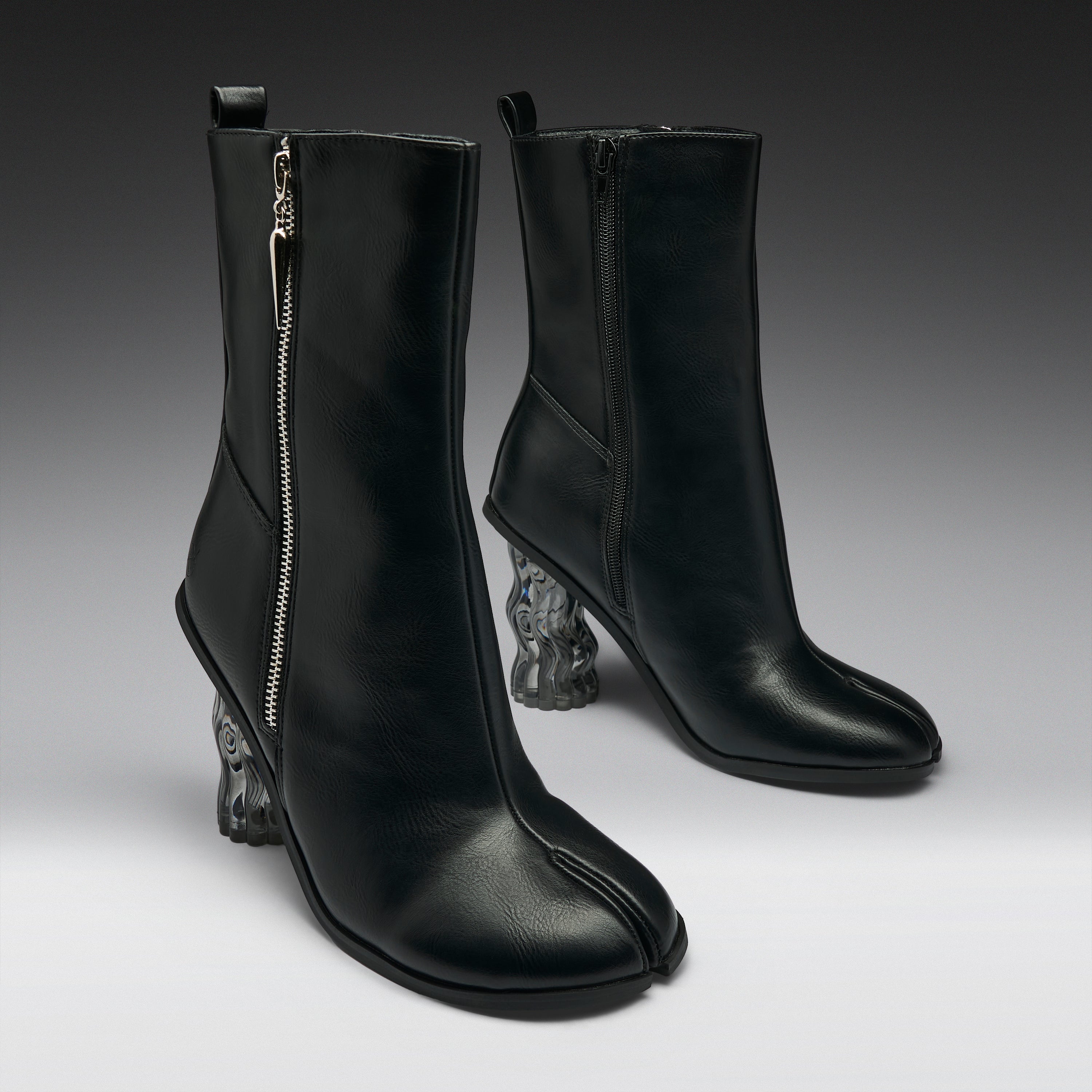 A pair of black leather ankle boots with a distinctive split toe and sculptural clear resin animal-head heels, shown against a dark gray studio background.