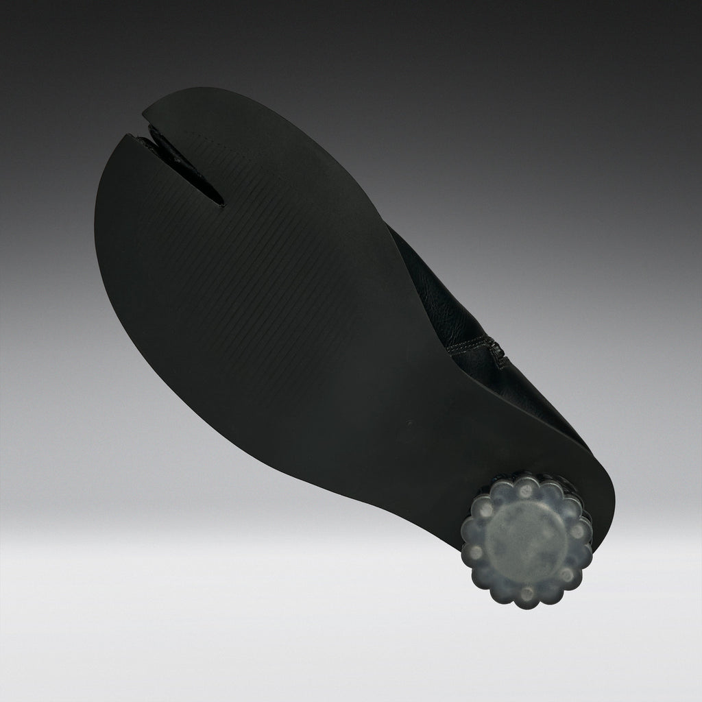 A black split-toe shoe sole with a textured surface and a translucent gray decorative end cap, shown on a dark-to-light gray gradient background.