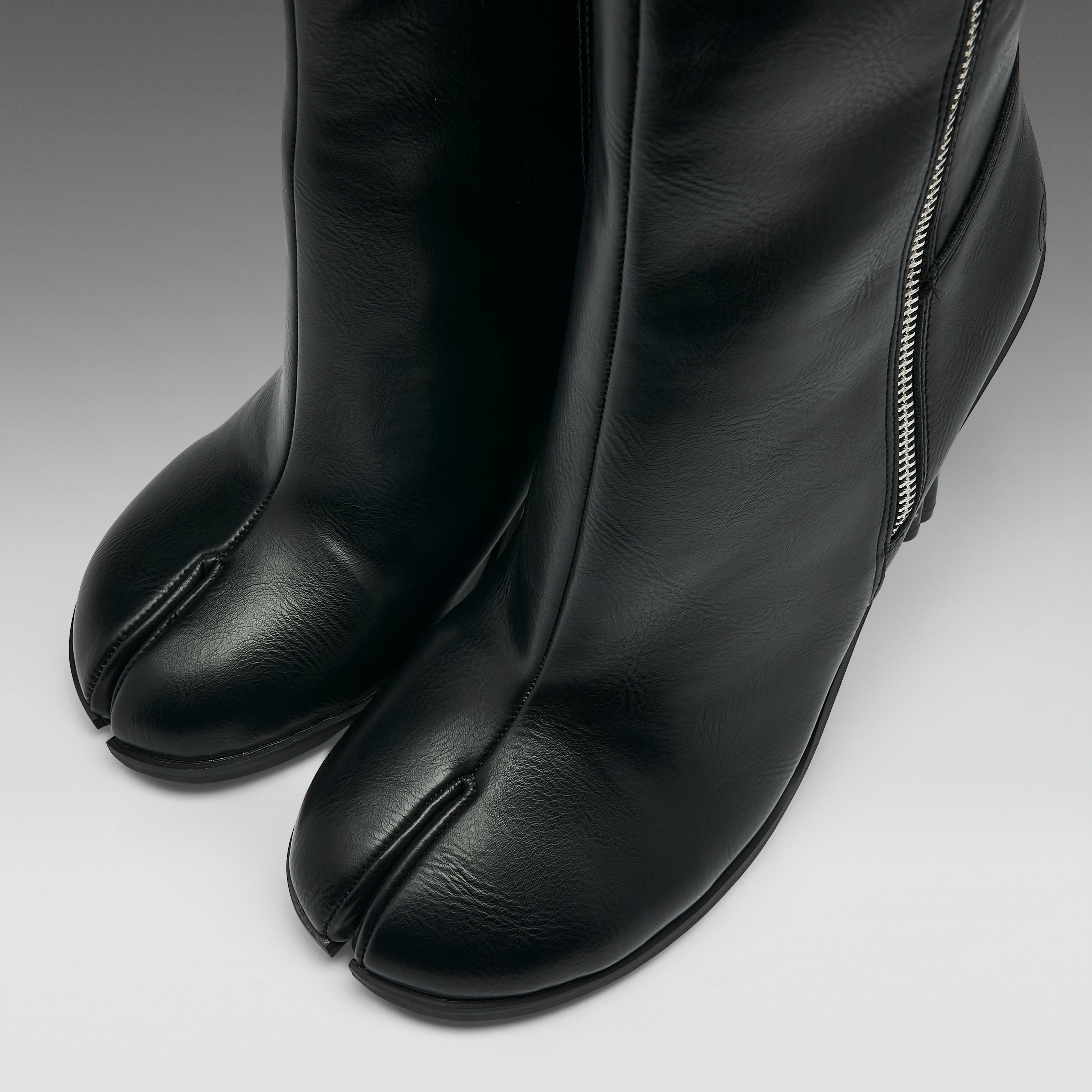 Close-up of a pair of black leather tab-cloth boots with a side zipper, shown on a neutral gray background.