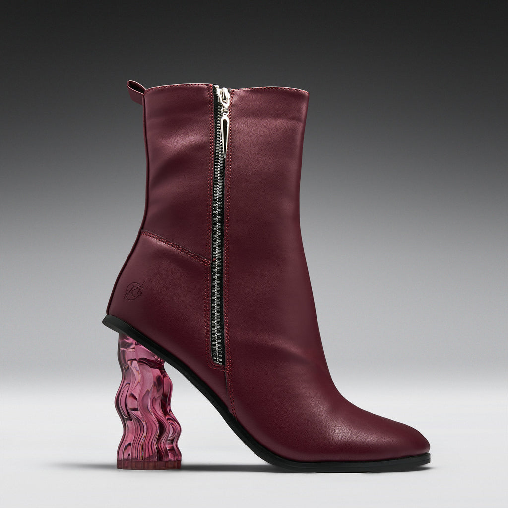 A single women's ankle boot in burgundy leather with a silver side zipper, a chunky wavy transparent pink block heel, and a black outsole, shown on a dark-to-light gray gradient studio background.