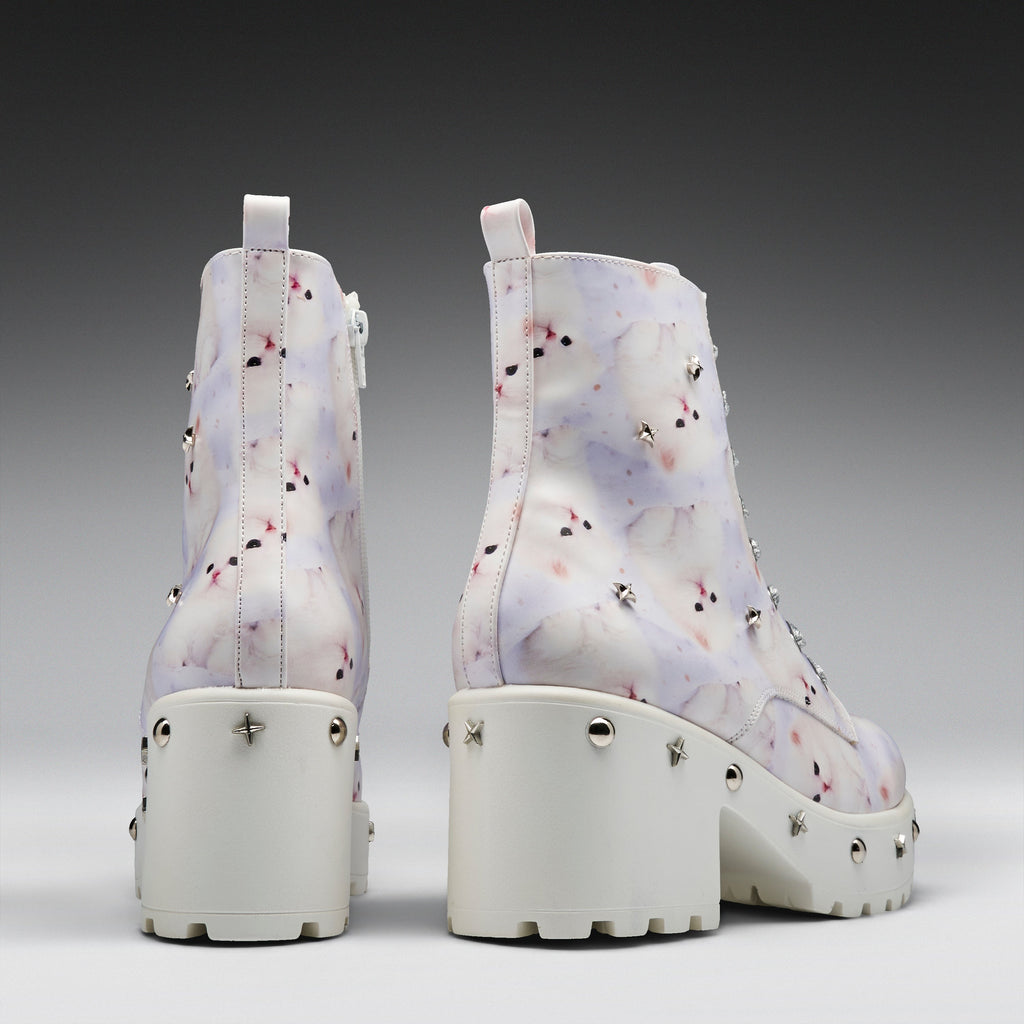 A pair of chunky platform ankle boots shown from the back, featuring a white base with a light purple and pink marble pattern, studded details, and thick white platform heels.