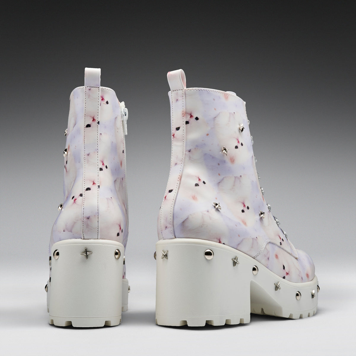 A pair of chunky platform ankle boots shown from the back, featuring a white base with a light purple and pink marble pattern, studded details, and thick white platform heels.