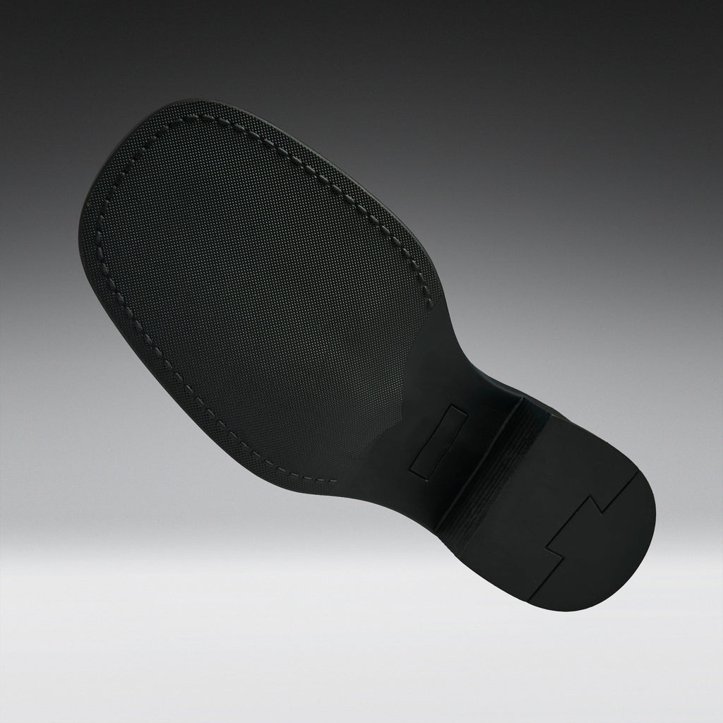A black textured shoe sole with visible stitching and molded tread details, shown floating against a dark-to-light gray gradient background.