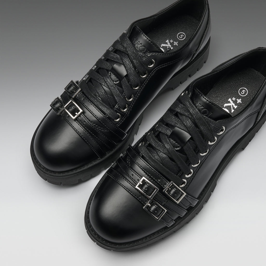 A pair of black leather lace-up shoes with decorative buckle straps on the sides, shown on a clean gray gradient background.