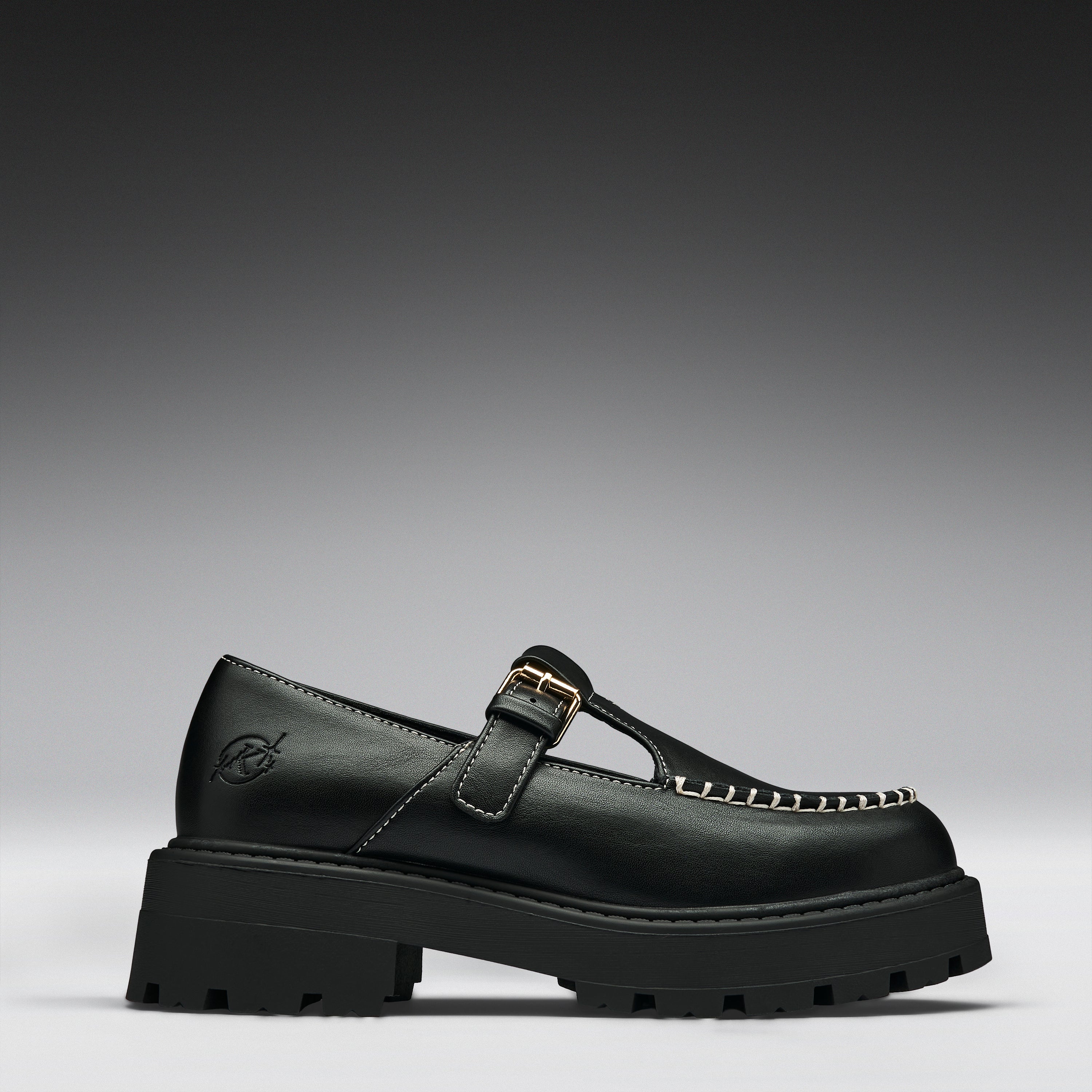 A single black leather Mary Jane loafer with a chunky lug sole, a gold buckle strap, and decorative gold stitching on the toe, shown against a dark gray gradient background.