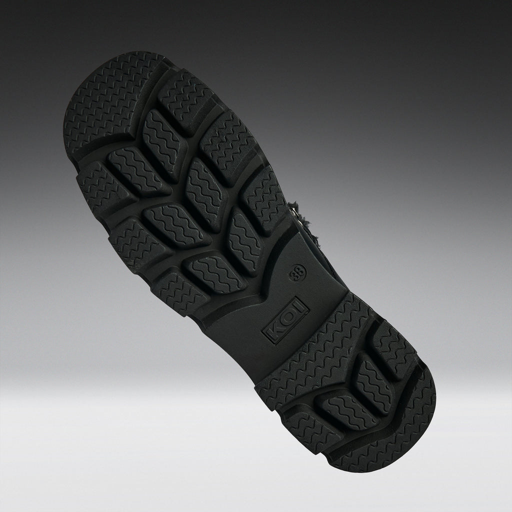A close-up of a black textured shoe sole, showing the tread pattern and embossed K-Swiss logo, set against a dark gray gradient background.