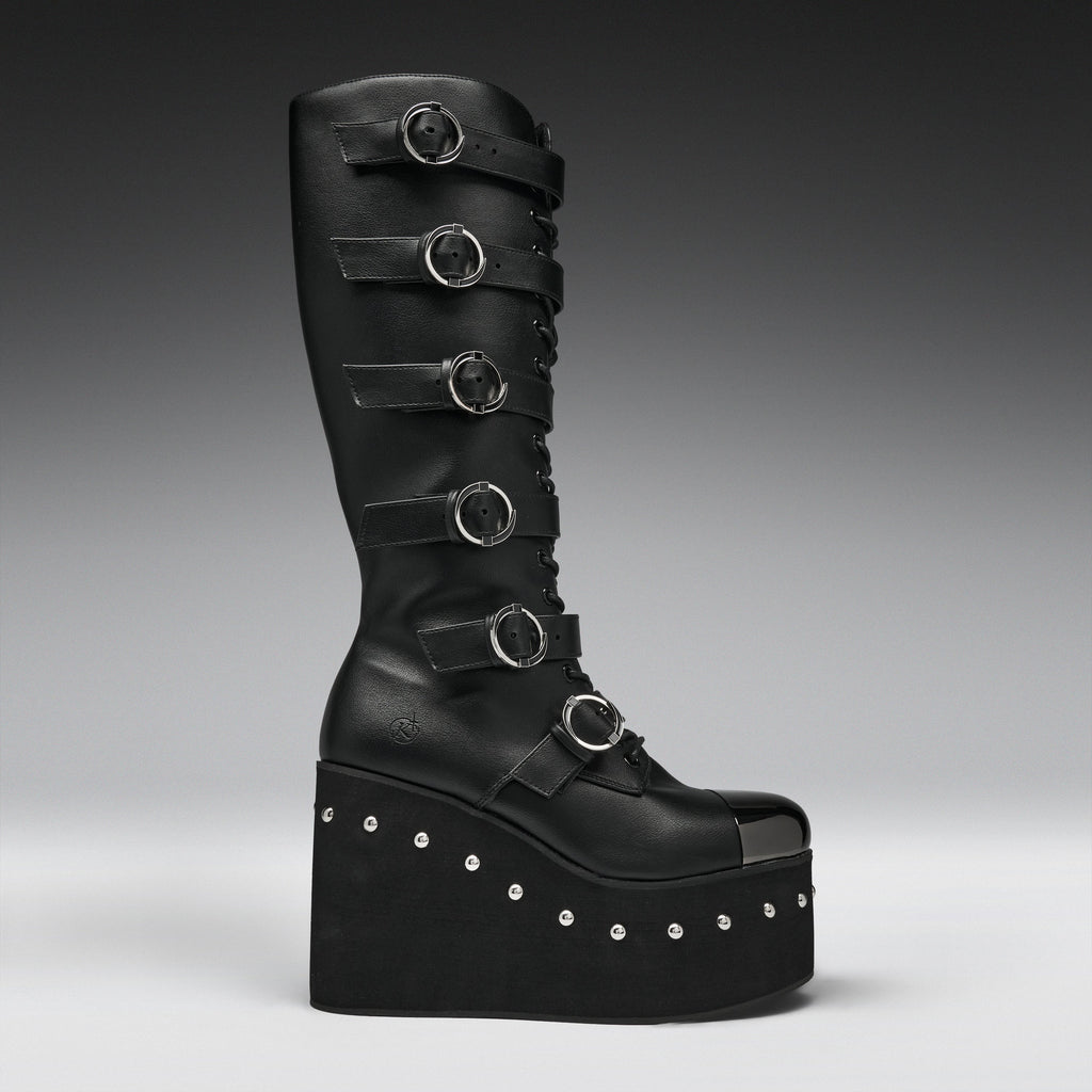 A tall black leather platform boot with multiple horizontal strap details and silver-tone circular buckles, photographed against a dark gray gradient studio background.