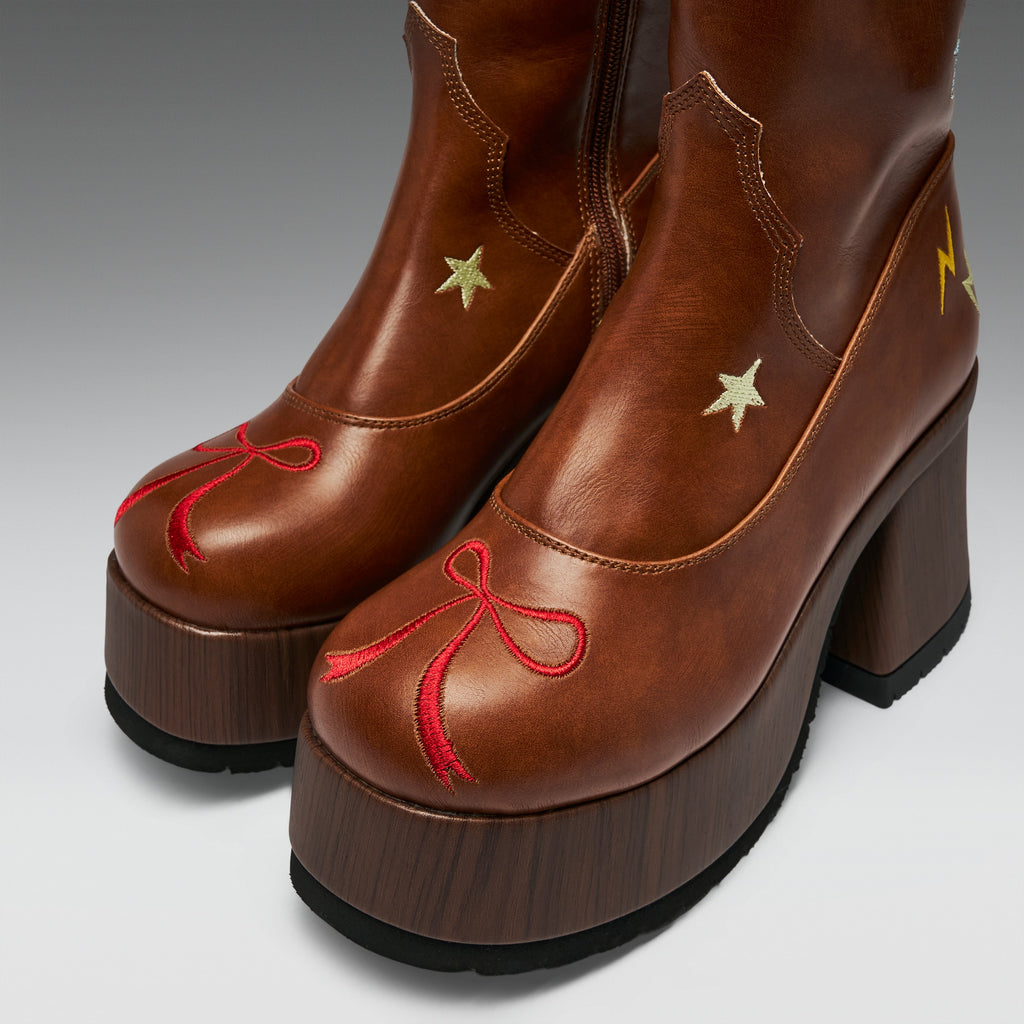 A pair of brown leather platform ankle boots with chunky dark brown wooden-look platform soles. The boots feature decorative embroidered details, including a red bow on the toe, gold stars on the sides, and a small yellow lightning bolt near the heel.