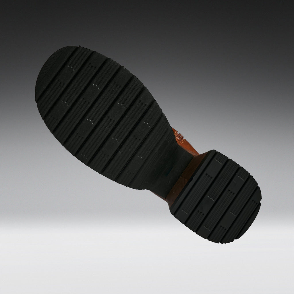A close-up of a black rubber boot sole with deep grooves and a brown heel, shown against a dark-to-light gray gradient background.