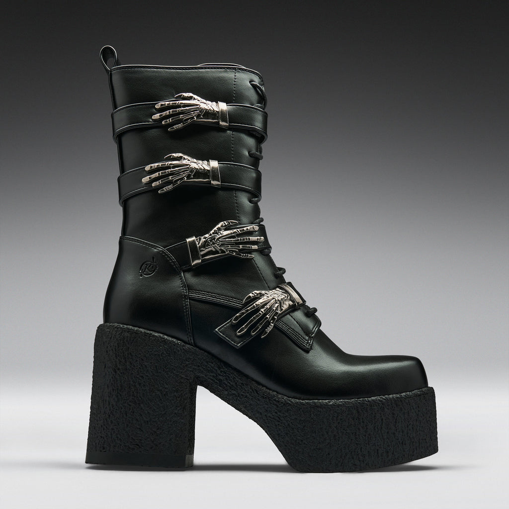 A black leather ankle boot with a chunky platform sole and high block heel, decorated with three silver metallic skeleton hand embellishments on the straps, shown against a dark gray gradient background.