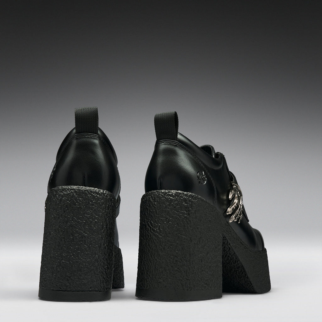 Black leather platform ankle boots with chunky textured block heels and silver chain details, shown from the back on a dark gray gradient background.