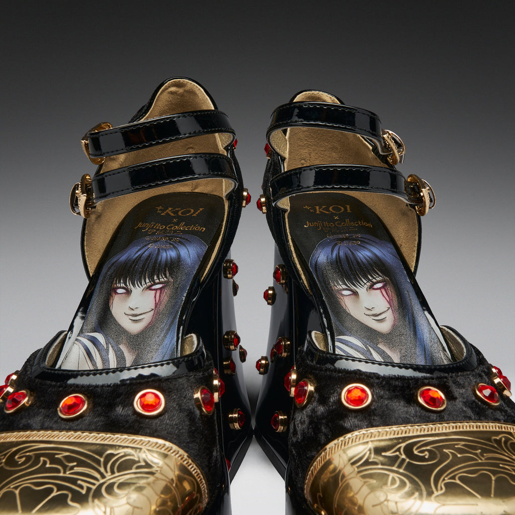 A pair of black and gold high-heeled platform shoes with red gem accents and an illustrated anime-style character printed on the insole, photographed against a dark gray gradient background.