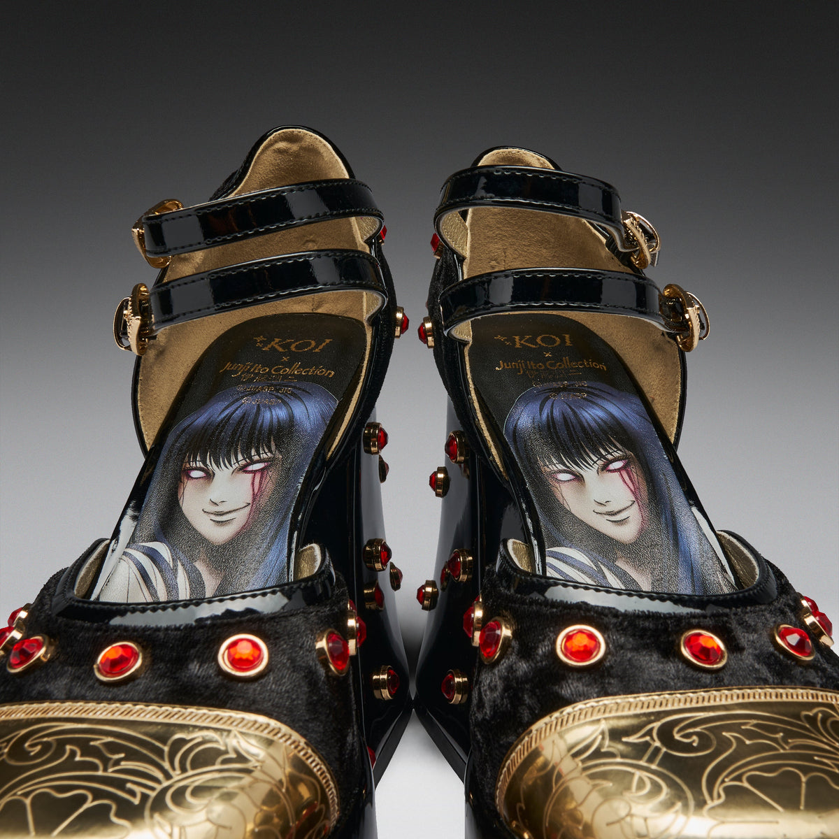 A pair of black and gold high-heeled platform shoes with red gem accents and an illustrated anime-style character printed on the insole, photographed against a dark gray gradient background.