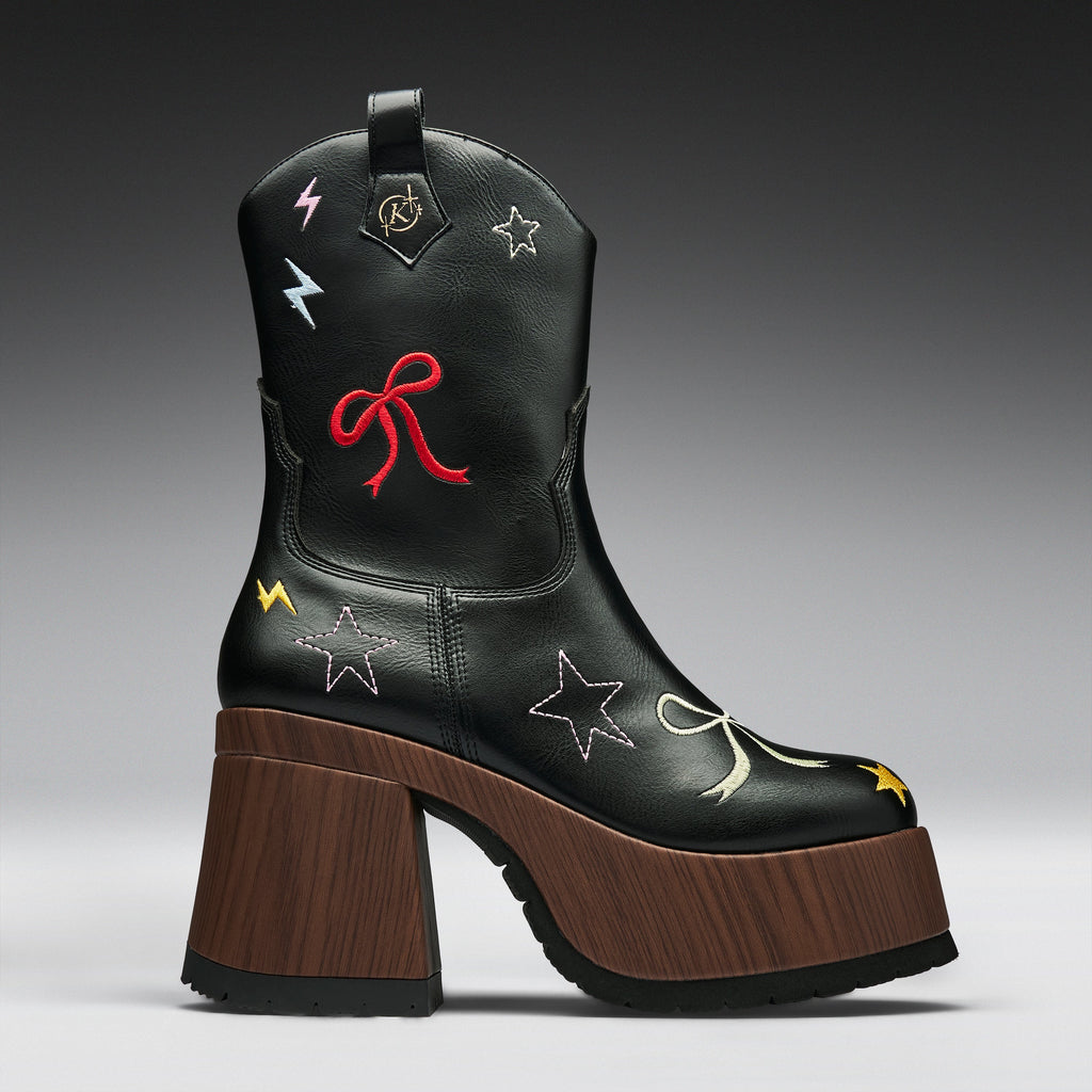 A black leather cowboy boot with a chunky brown wooden block heel and platform sole, decorated with embroidered stars, bows, and lightning bolts in red, yellow, and white.