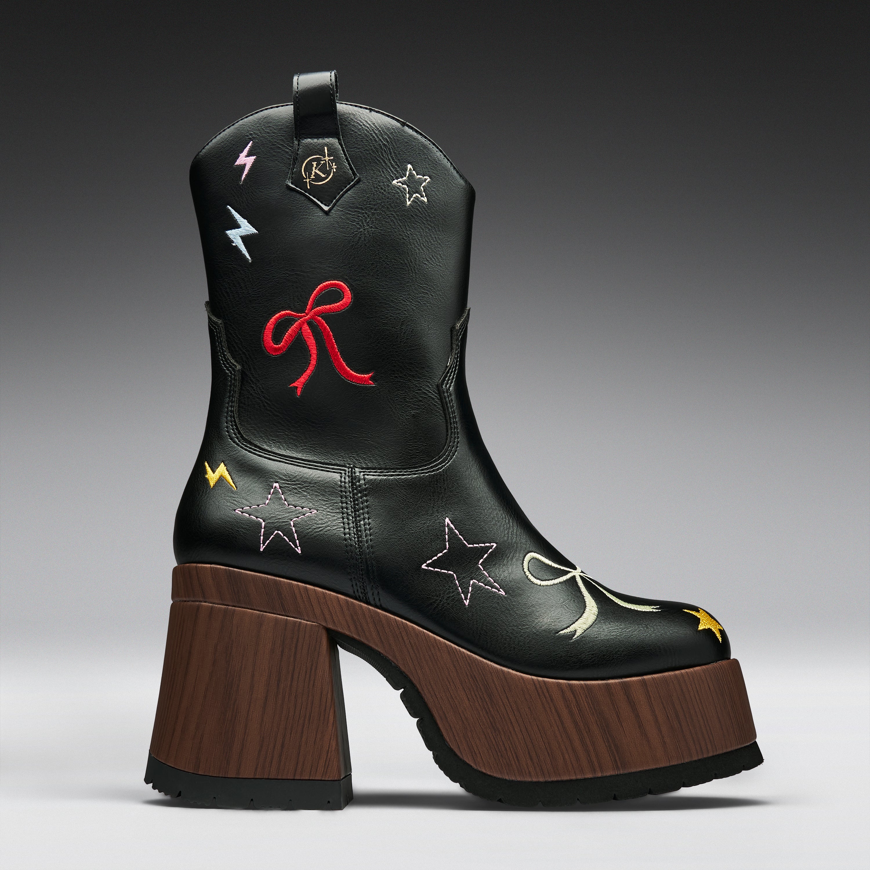 A black leather cowboy boot with a chunky brown wooden block heel and platform sole, decorated with embroidered stars, bows, and lightning bolts in red, yellow, and white.