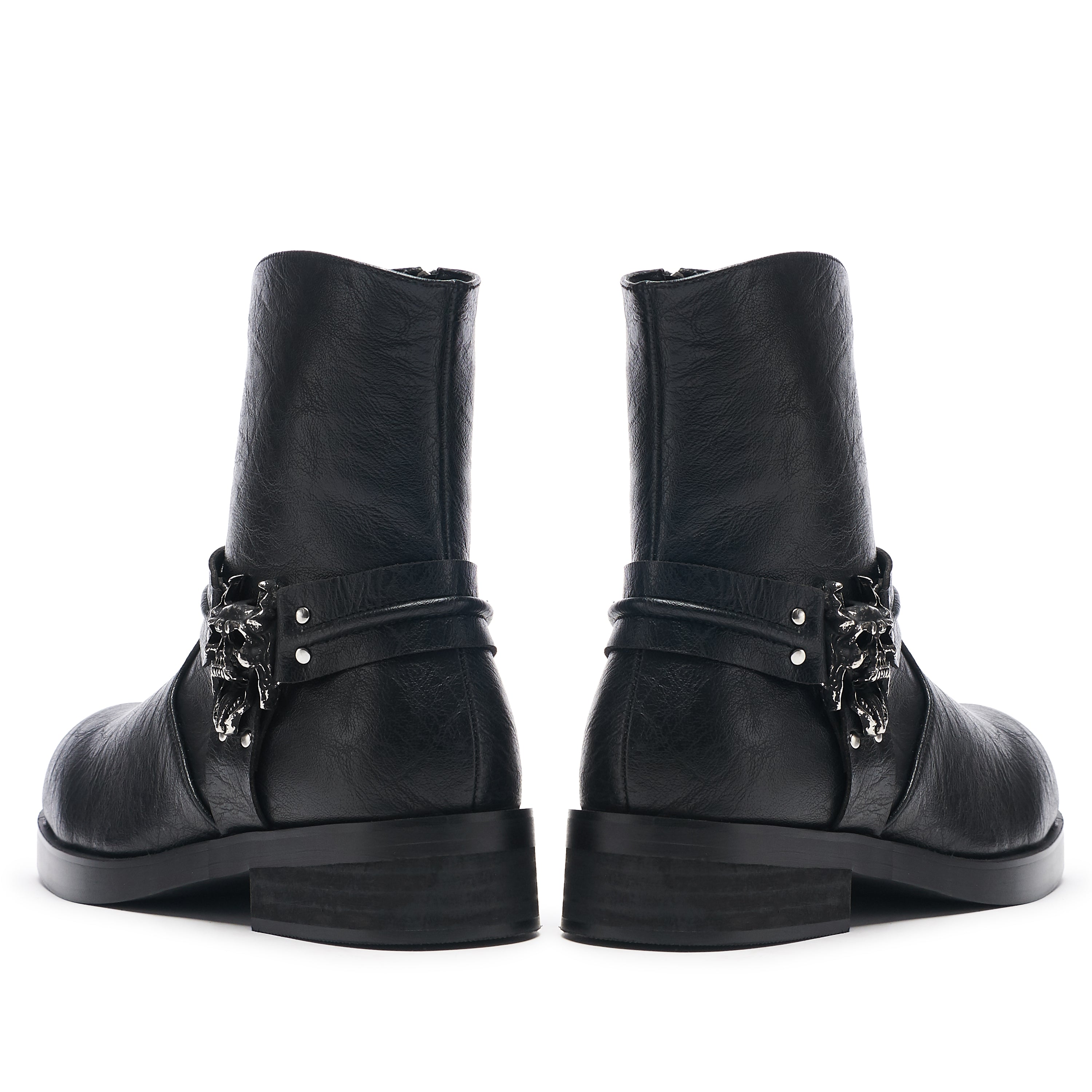 A pair of vintage black leather biker boots with stacked hardware and a decorative element on the heel.