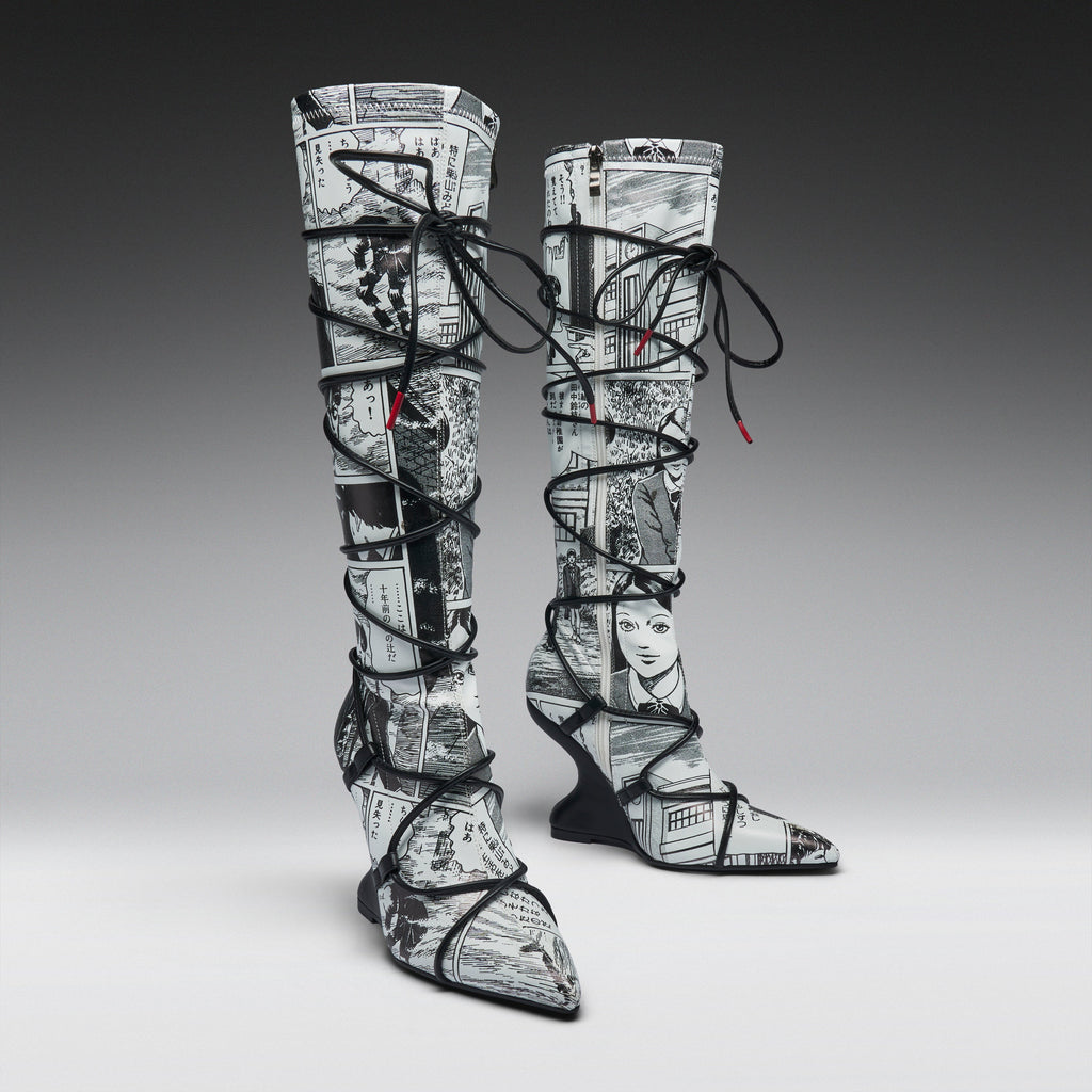 A pair of thigh-high pointed-toe boots with a black and white newspaper collage print, wrapped in black lace up to the ankles, shown on a gray gradient studio background.