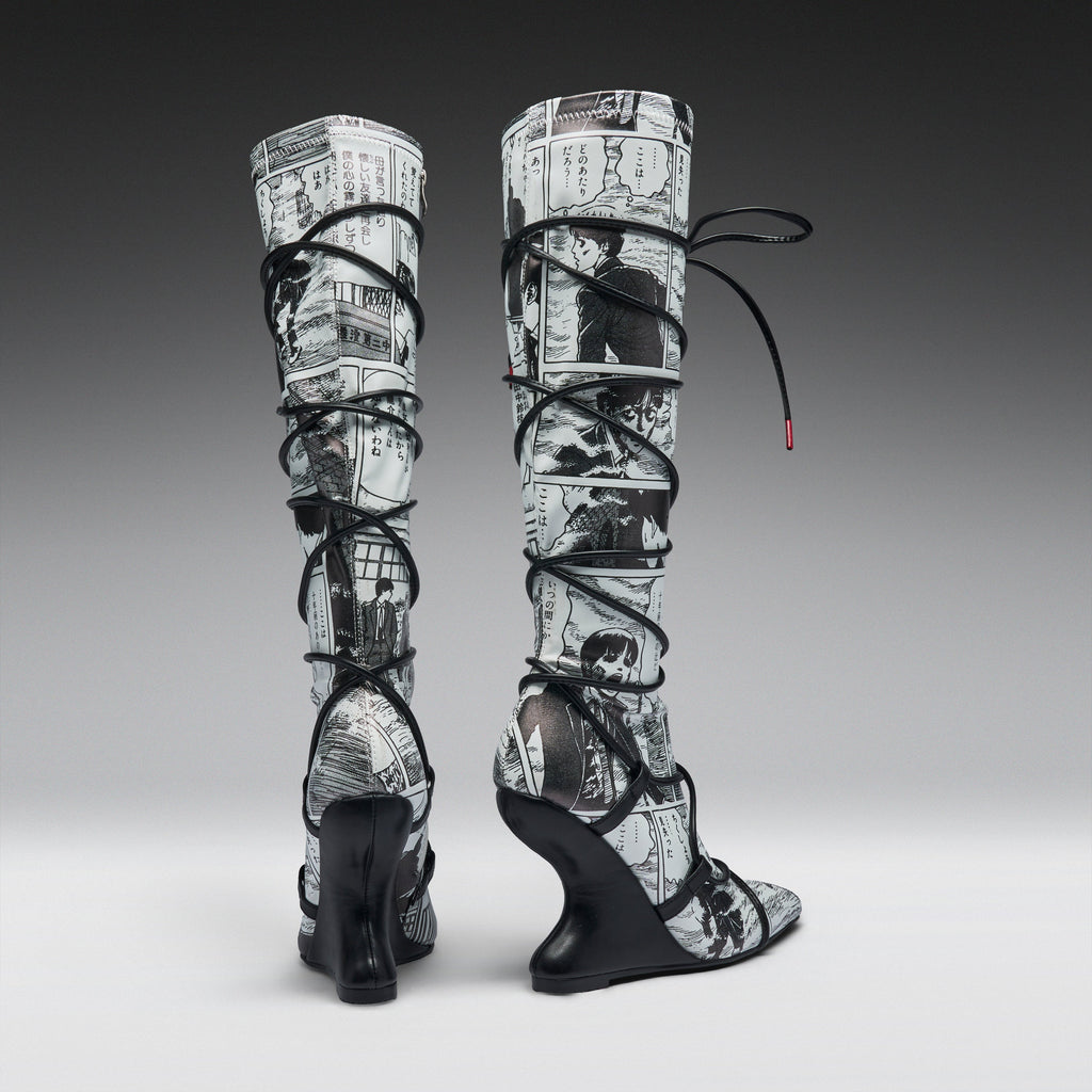 A pair of high-heeled, over-the-knee boots featuring a black and white newspaper print pattern wrapped around the shafts, with black lace-up straps and wedge heels, shown against a gray gradient studio background.