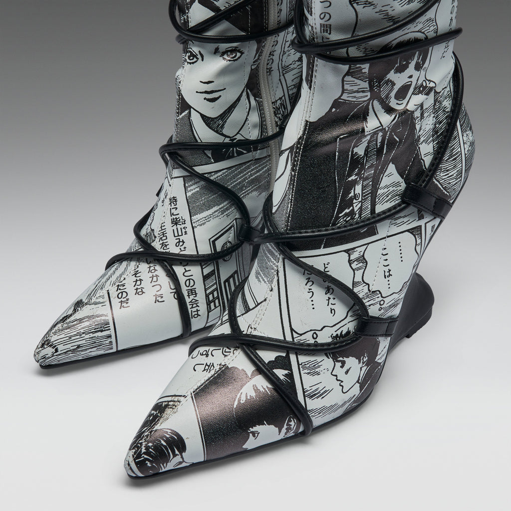A pair of pointed-toe high-heeled boots featuring a black and white manga comic book print with black lace-up wrap details, shown on a neutral gray background.