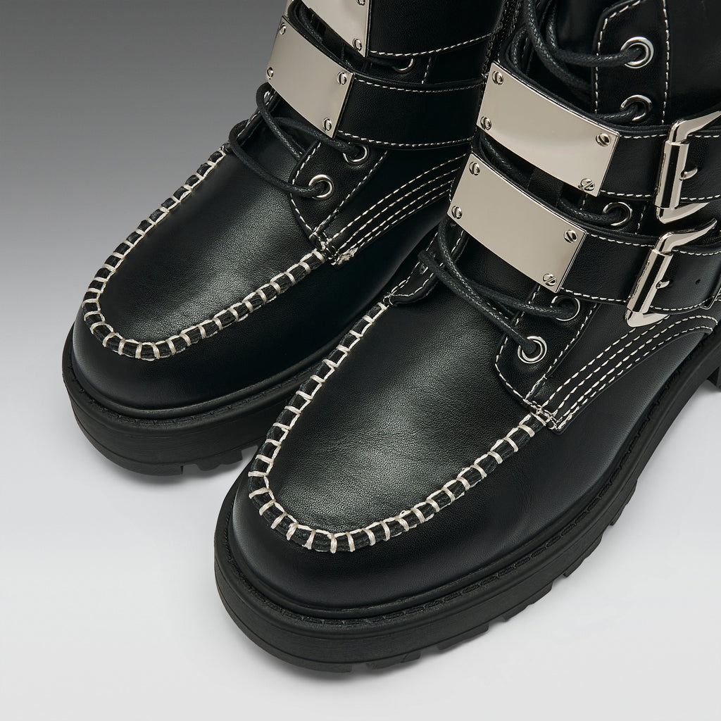 Black leather lace-up boots with silver metal strap accents, white contrast stitching, and thick black soles, shown on a light gray background.