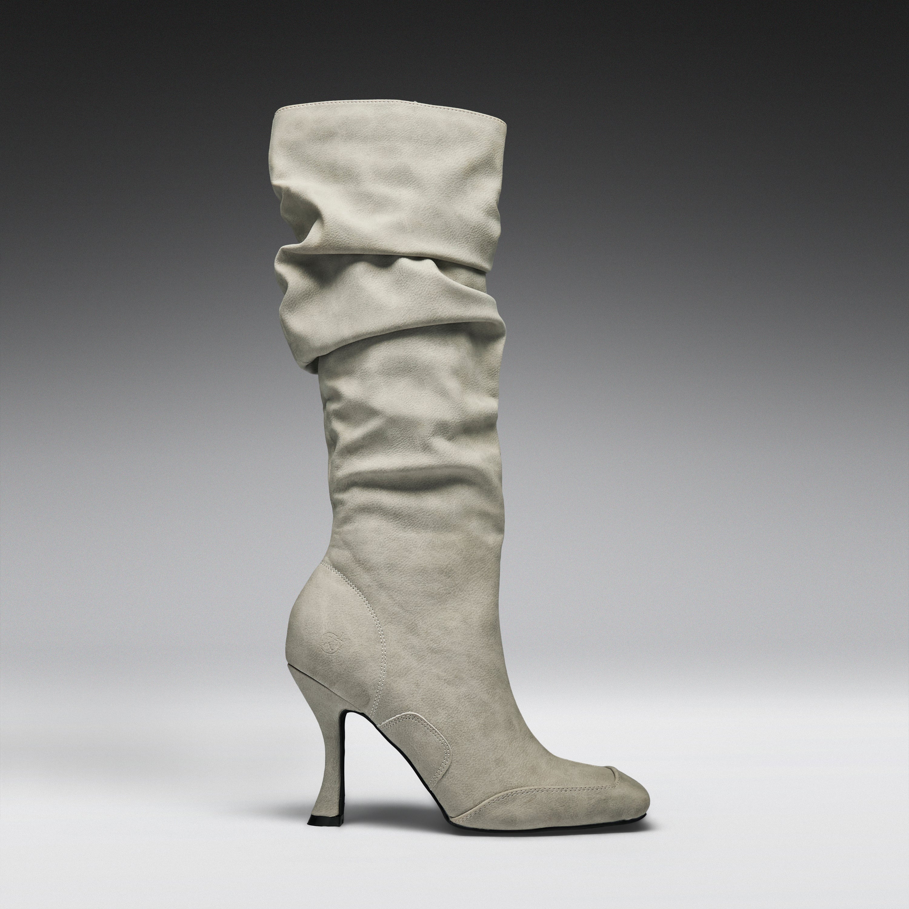 A single knee-high slouch boot in light gray suede, featuring a pointed toe and a slim stiletto heel, shown against a dark-to-light gray studio gradient background.
