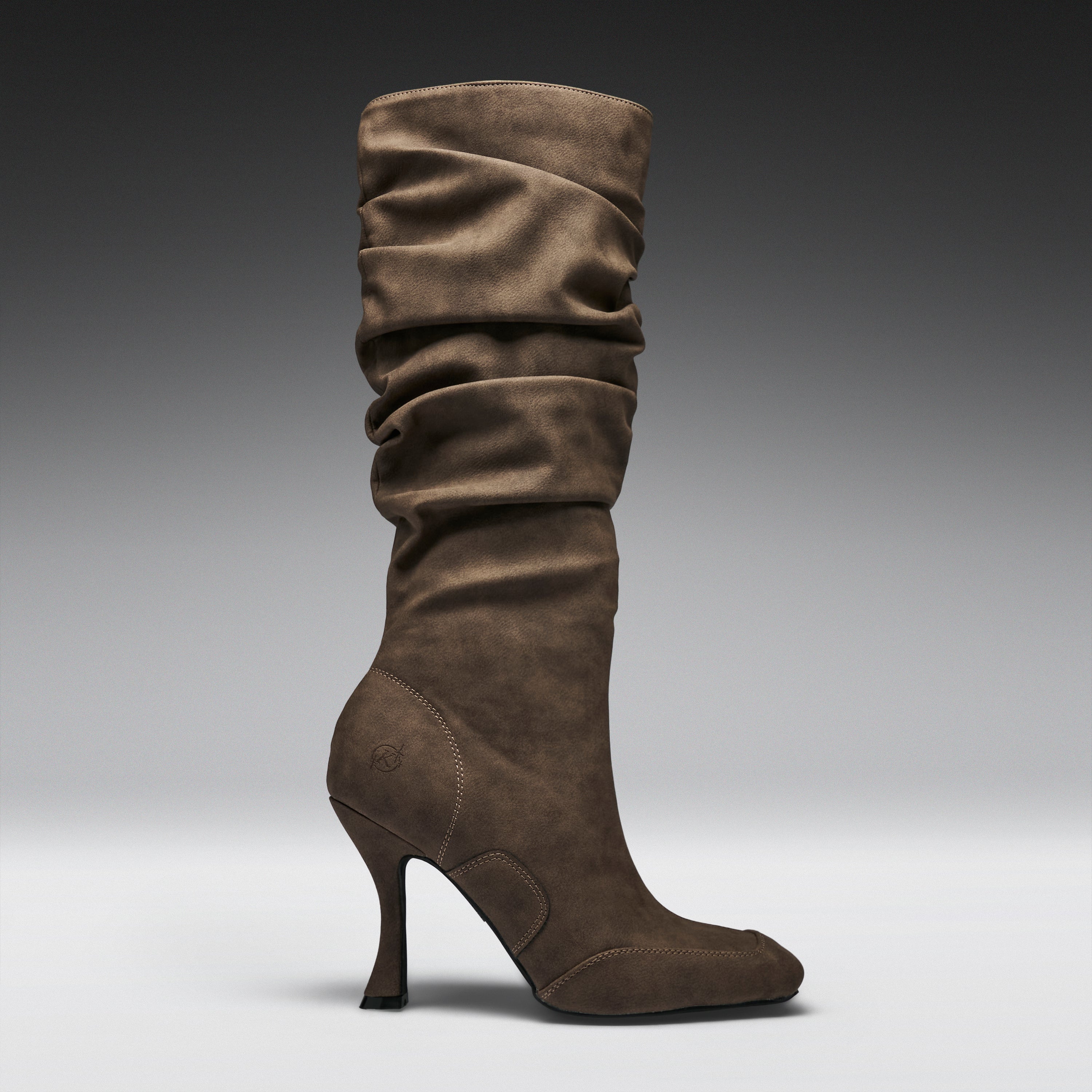A single mid-calf heeled boot in brown suede, shown in profile against a dark-to-light gray gradient studio background.