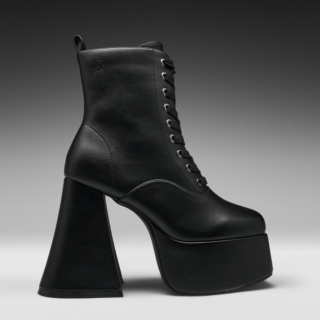A single black leather lace-up ankle boot with a dramatic high block heel and platform sole, shown in profile against a dark gray gradient studio background.