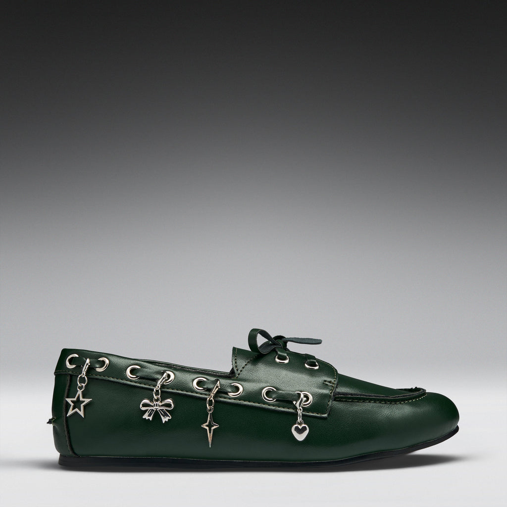 A dark green leather moccasin-style loafer with silver-tone decorative charms hanging from the eyelets, photographed on a clean gray gradient studio background.