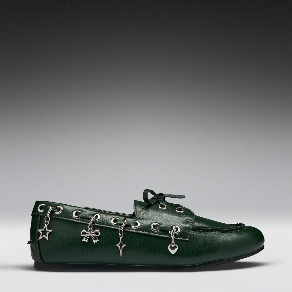A dark green leather moccasin-style loafer with silver-tone decorative charms hanging from the eyelets, photographed on a clean gray gradient studio background.
