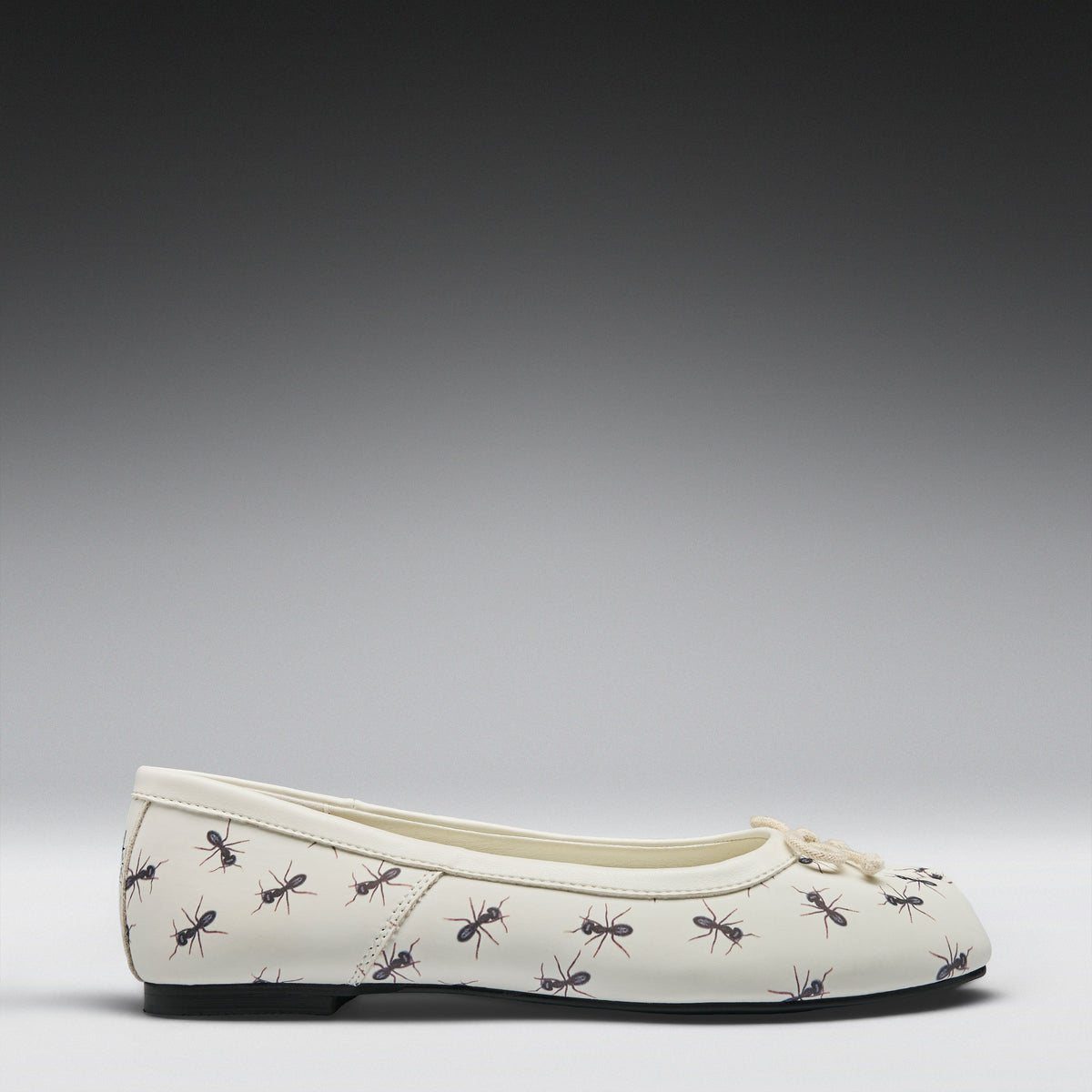 A single cream-colored ballet flat shoe with a repeating pattern of black and brown ants, shown in profile against a dark-to-light gray gradient studio background.