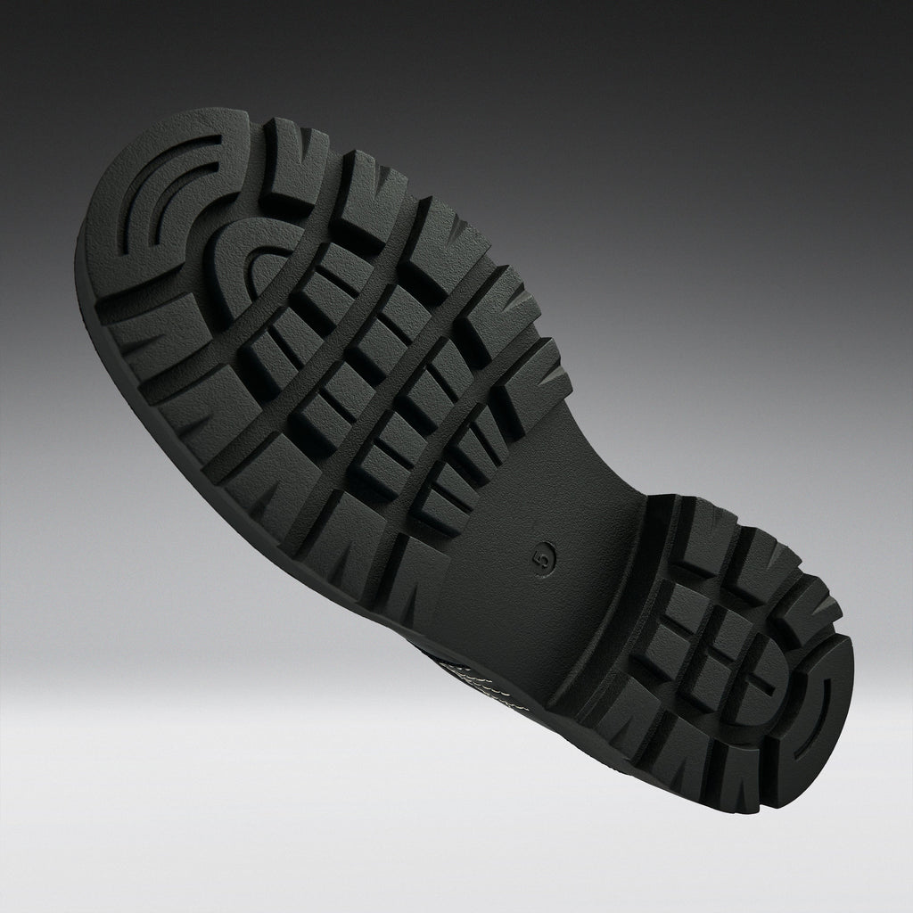 A close-up of a black rubber shoe sole with deep lugs and a textured tread pattern, shown against a dark-to-light gray gradient background.