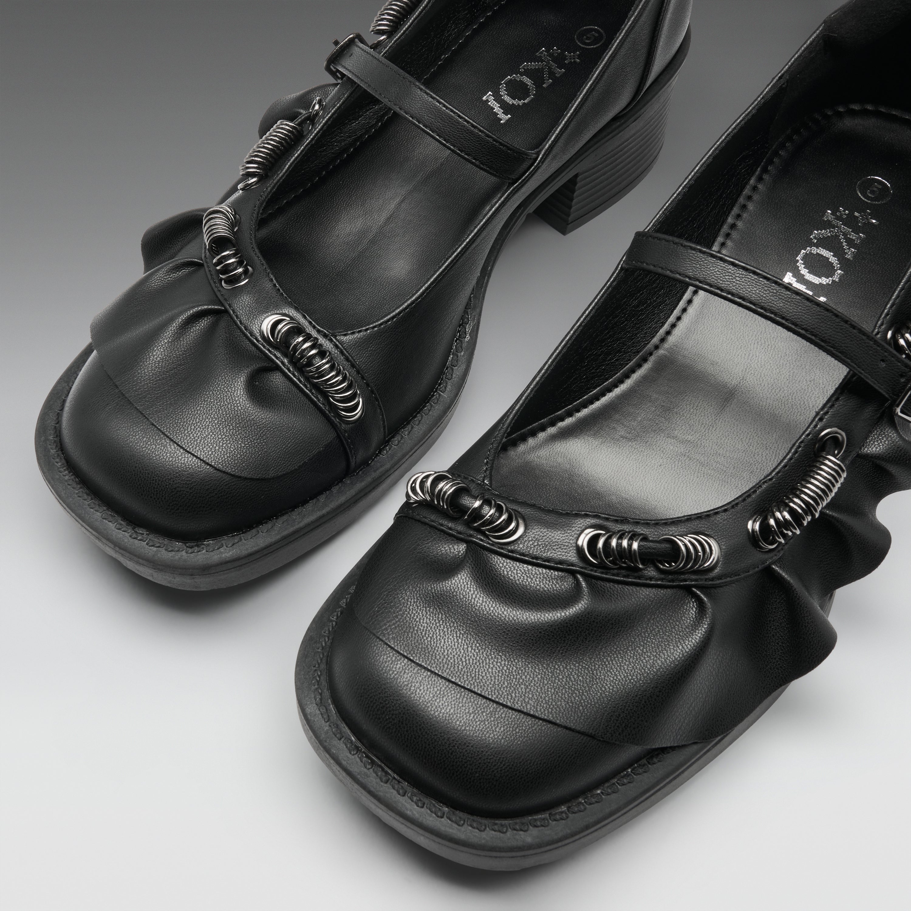 A pair of black Mary Jane-style shoes with textured spiral embellishments on the straps, shown on a neutral gray background. The brand name 'IOKZO' is visible on the insole.