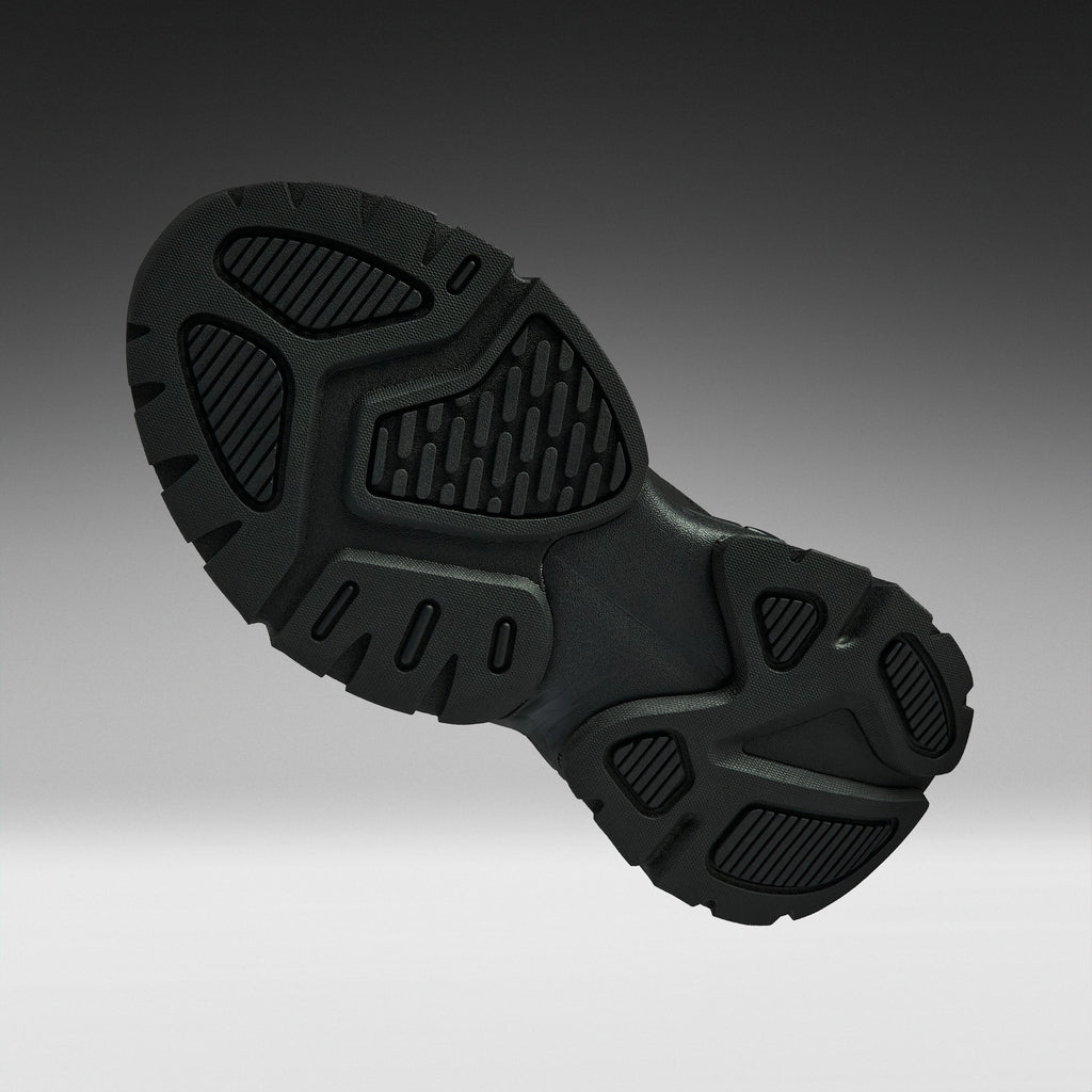 A close-up of a black athletic shoe's textured outsole, shown from a side angle against a dark-to-light gray gradient background.