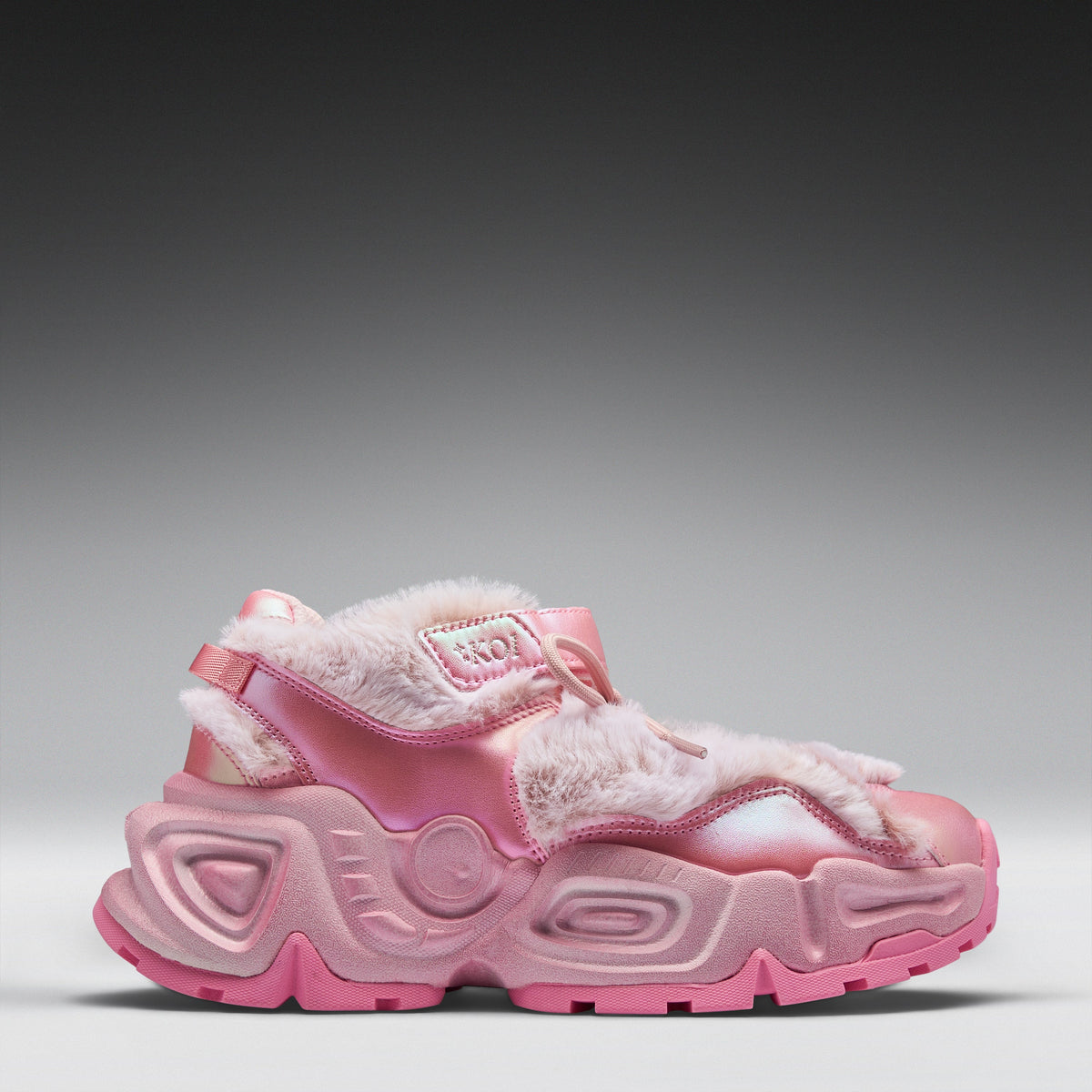 A pink chunky platform sneaker with faux fur trim and glossy pink straps, shown in a side profile against a gray gradient background.