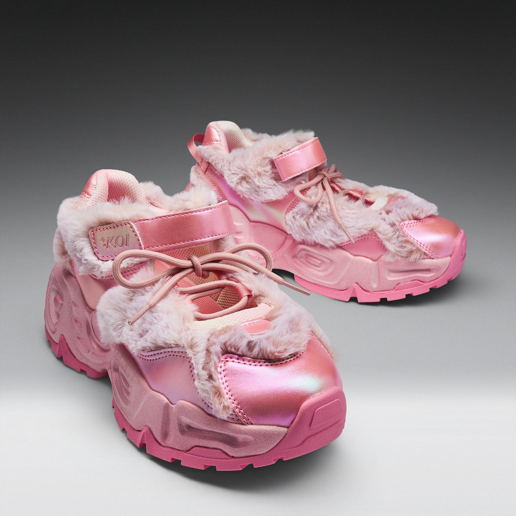 A pair of chunky pink sneakers with shiny metallic pink panels, fuzzy faux-fur trim, and pink laces, photographed on a clean gray studio background.