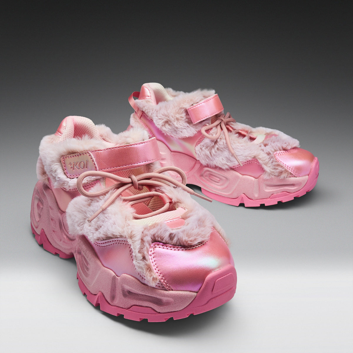 A pair of chunky pink sneakers with shiny metallic pink panels, fuzzy faux-fur trim, and pink laces, photographed on a clean gray studio background.