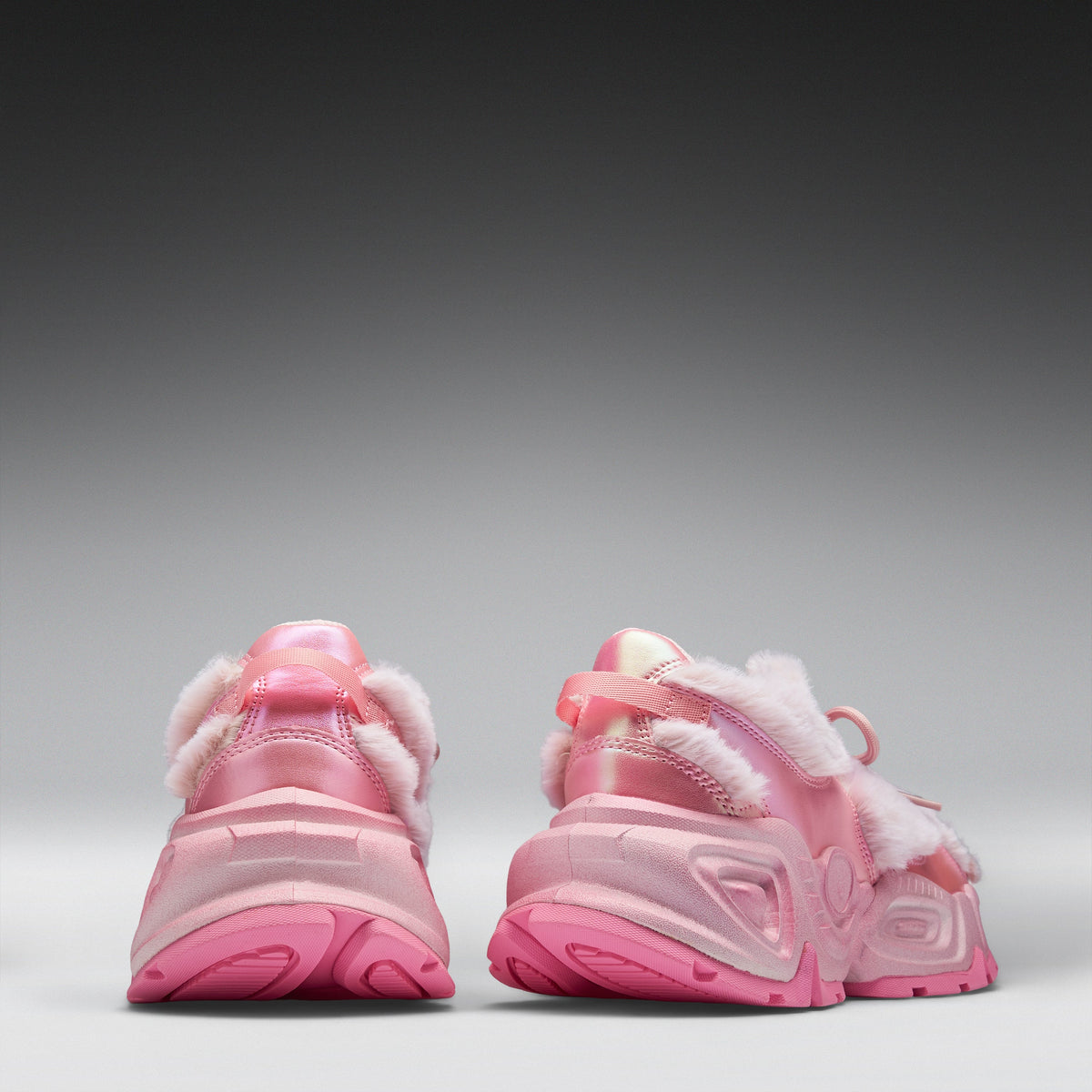 A pair of pink chunky sneakers shown from the back, featuring fuzzy white faux-fur trim and translucent pink soles, set against a dark-to-light gray gradient studio background.