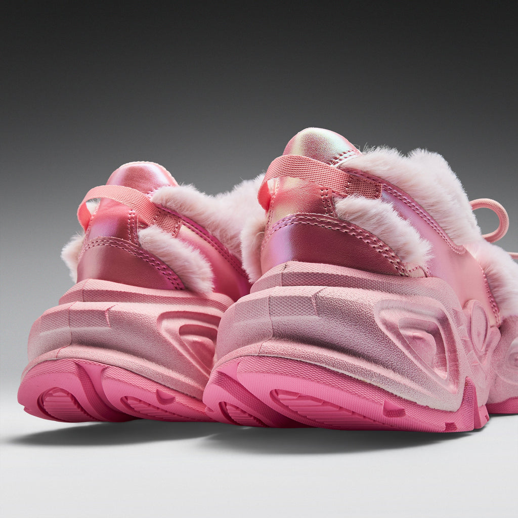 A pair of chunky pink winter sneakers with fluffy white faux-fur trim and glossy metallic pink uppers, shown from a low angle against a dark-to-light gray gradient background.