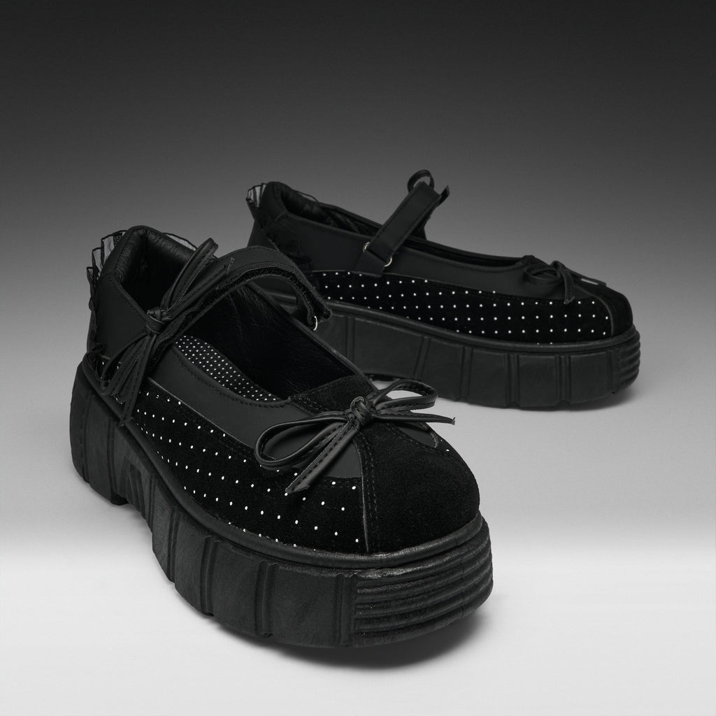 A pair of black Mary Jane platform shoes with textured soles, black mesh side panels, and silver studs, displayed on a gray gradient studio background.