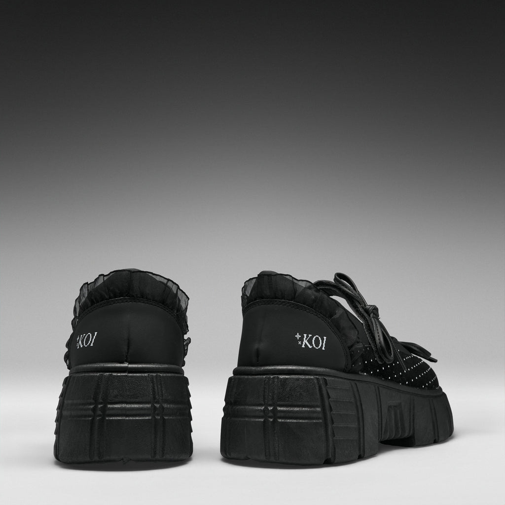A pair of black platform sneakers shown from the back, featuring chunky lug soles, black laces, and the brand name 'KOI' printed in white on the heel.